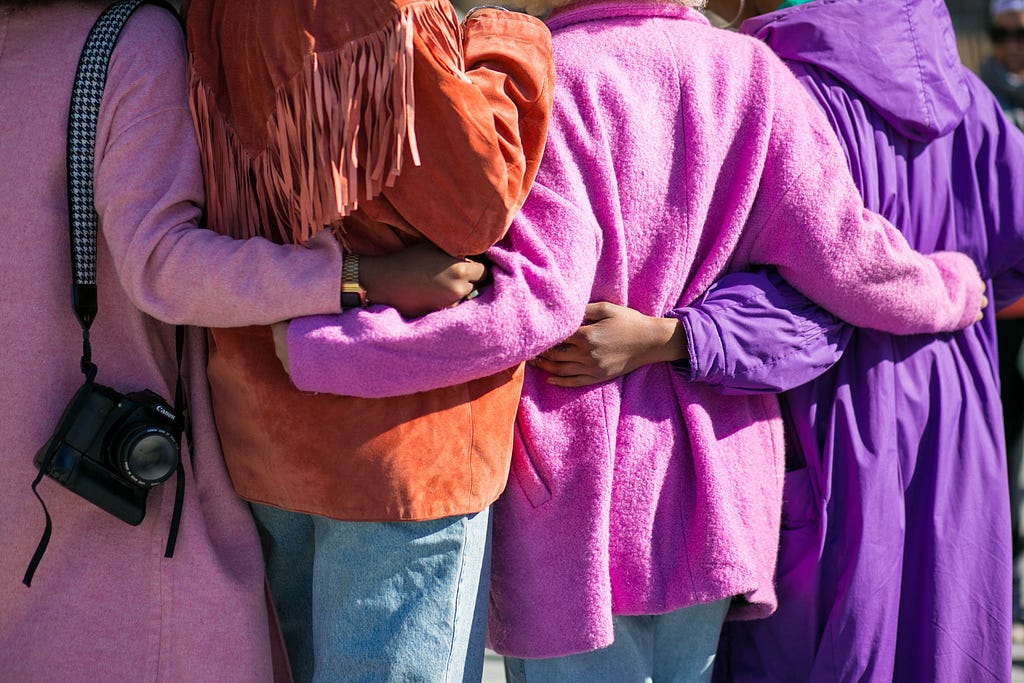 A group of women with their backs turned, holding each other at the waist.