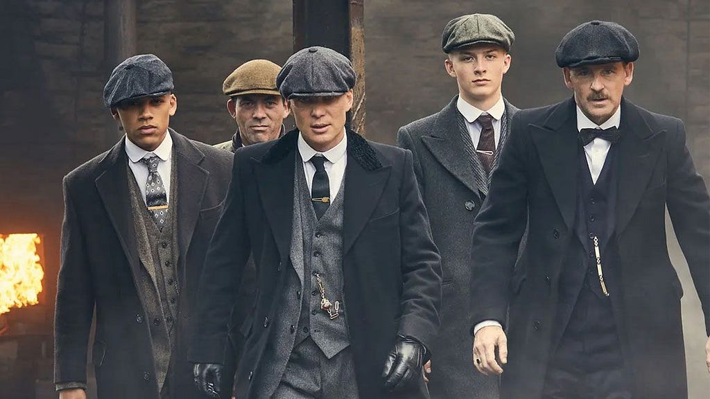 A group of men all dressed in suits, overcoats and newsboy caps