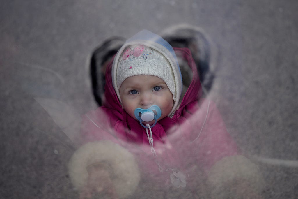 A child who fled the war from neighboring Ukraine looks through a bus window in Przemysl, Poland, Wednesday, March 9, 2022. (AP Photo/Daniel Cole)