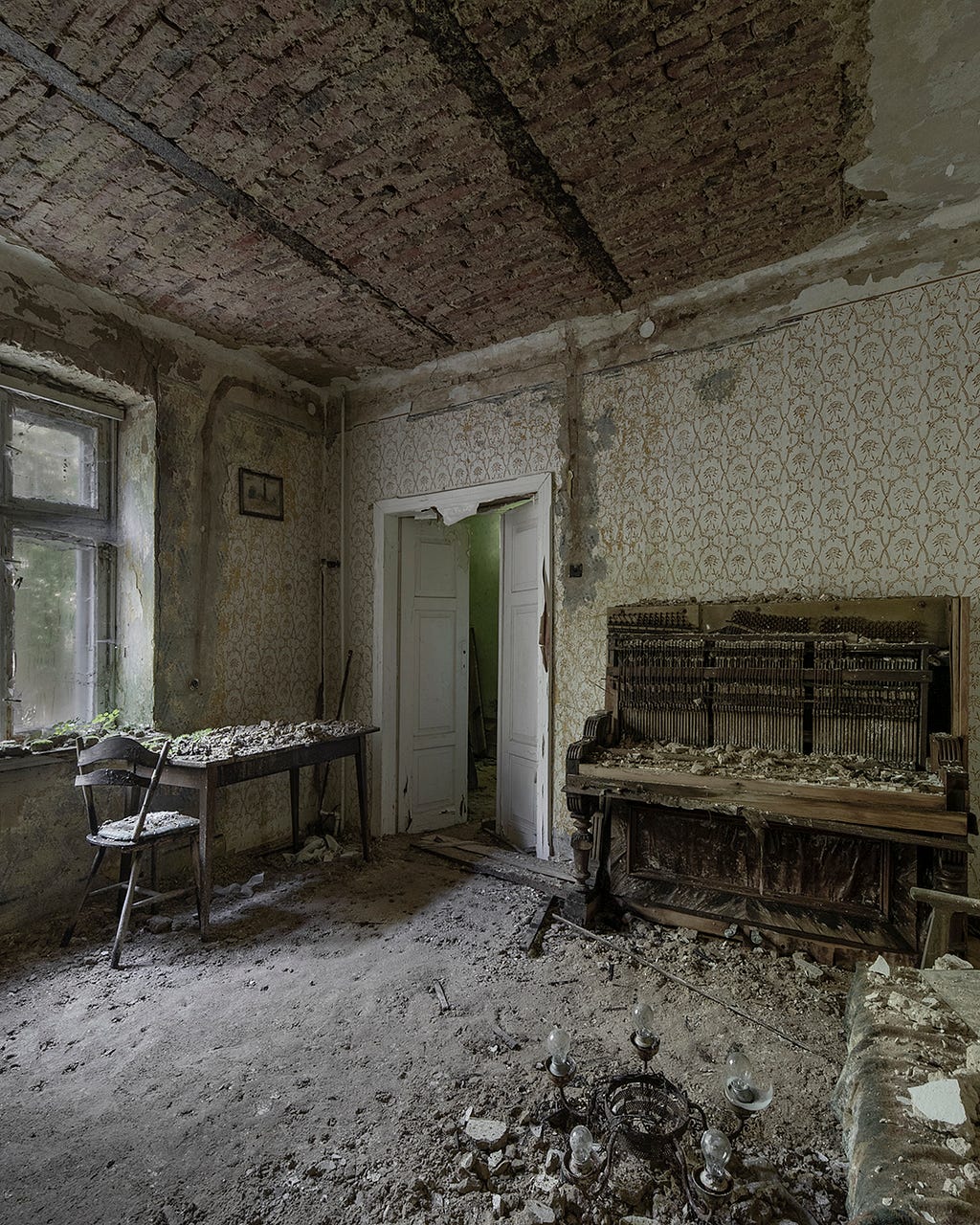 Interior of an abandoned house. In the photo there is a piano, table and a chair and wallpapers which are covered in mold.