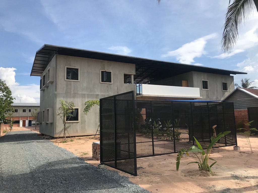 A concrete building. There is a steel fence and trees in front of the building.