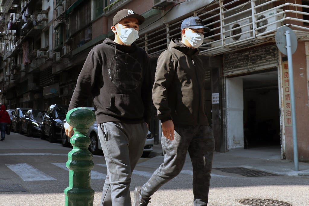 Two men walk together down the street with COVID-19 masks on.