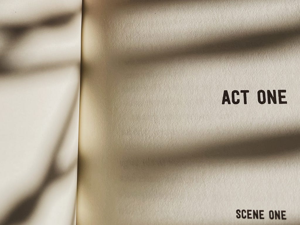a book is open. the pages are blank except for the words ‘Act one’ and then blow ‘scene one’
