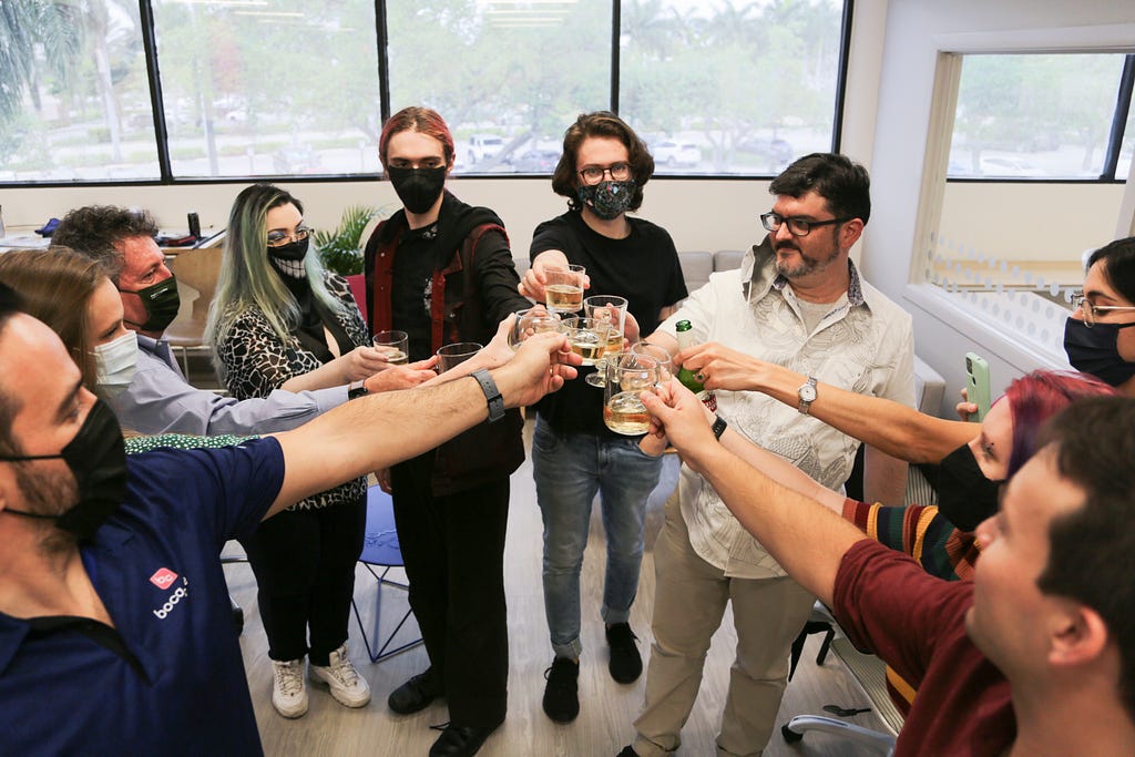 A group of 10 adults, students, instructors, and family, stand in a circle, glasses raised together, toasting to success.