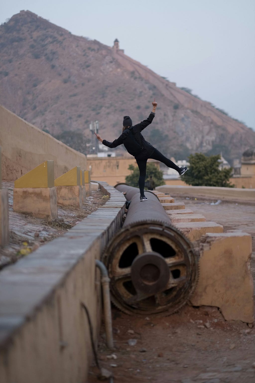 The back of a person balancing on one leg on top of a long pipe.