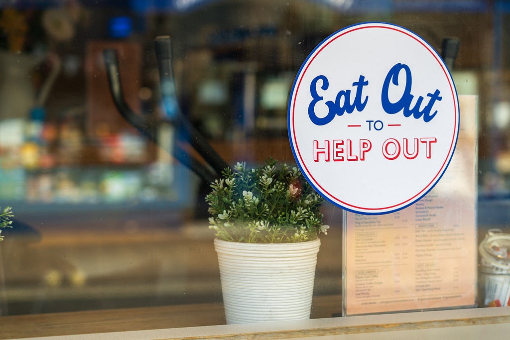 a sign in a restaurant window saying “Eat Out to Help Out”