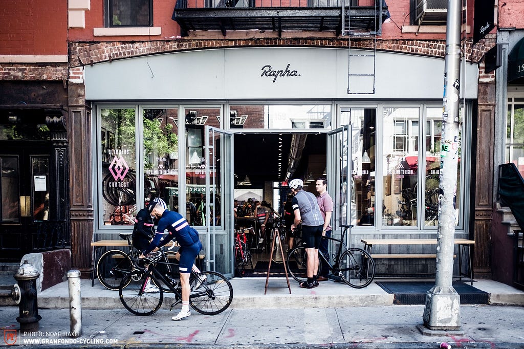 Vor einem Laden namens “Rapha” stehen zwei Rennradfahrer.