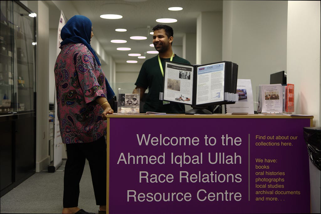 Two people chat behind a welcome desk in the Ahmed Iqbal Ullah RACE Centre.