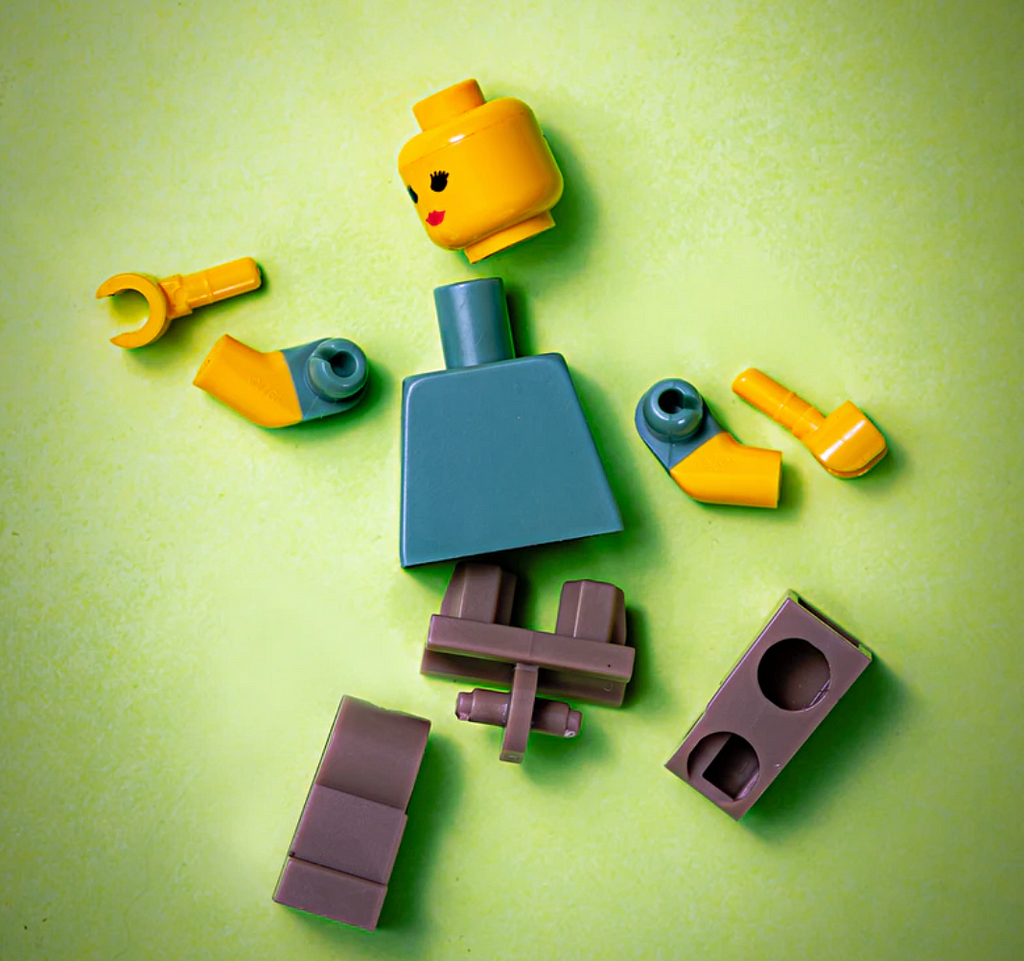 Imagem de um boneco de lego completamente desmontado sobre uma superfície verde.