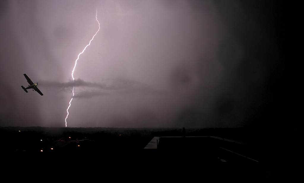 Photo of lightning in the sky behind a small airplane flying.