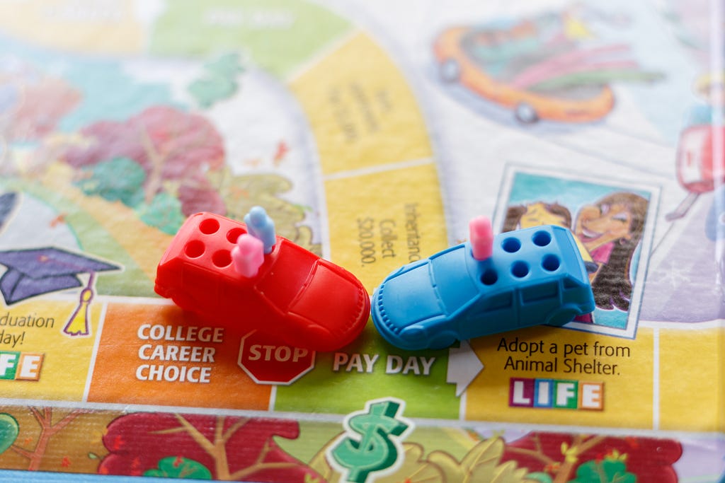 Photo depicting a car crash using the board and game pieces from The Game of Life