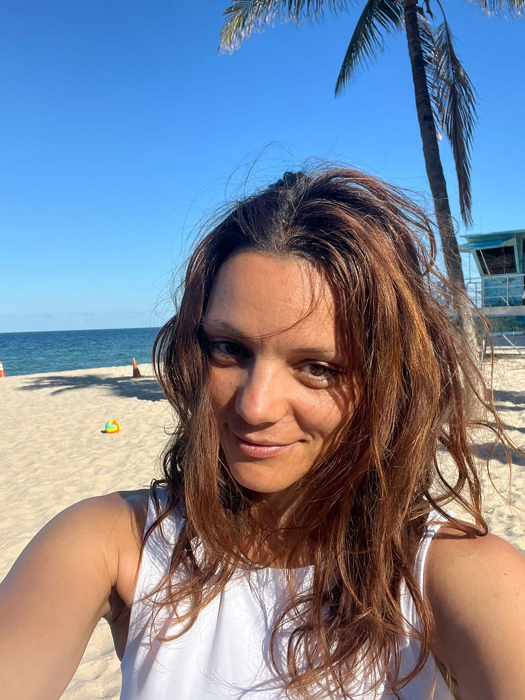 Beautiful Girl natural with wavy hair on a beach in Florida, with the sea and the beach behind. Smile with her eyes, good vibe and brown hair freelancer designer.
