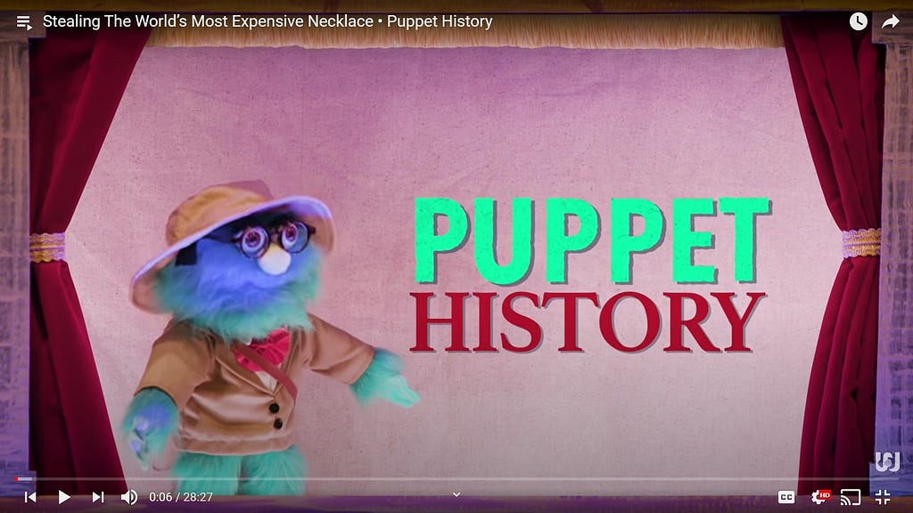 A blue puppet in a beige jacket with a red bowtie stands in a red and gold puppet theatre alongside the Puppet History Logo