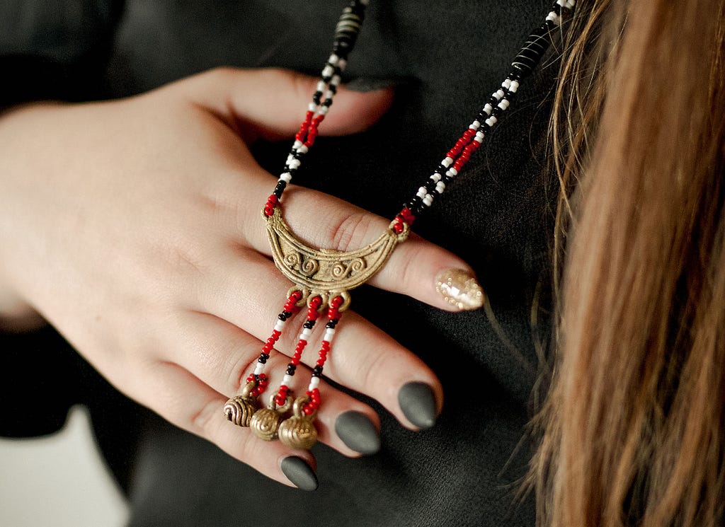 With the back of her hand, Alida holds a red, black, white, and gold necklace blessed by a Santero and honoring the West African orisha Eleggua.
