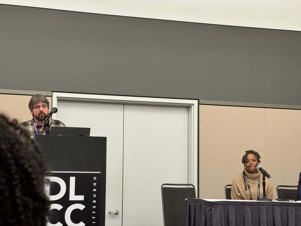 Michael kicks off the panel at the podium while Yolana scans the audience.