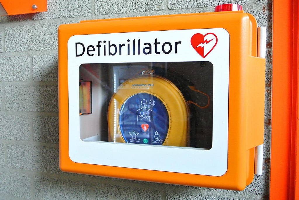 An orange defibrillator mounted on a grey brick wall