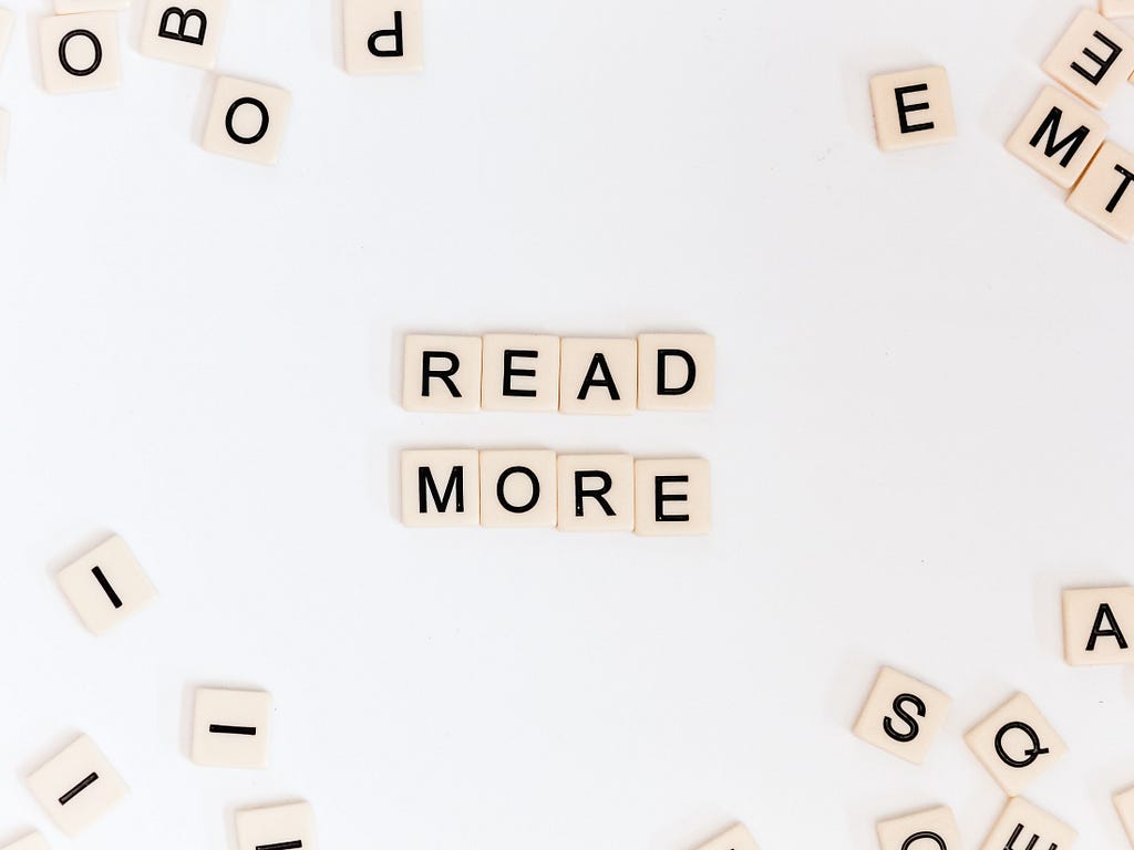 Scattered scrabble tiles on a plain white background, in the centre of the photo spelling out ‘read more’