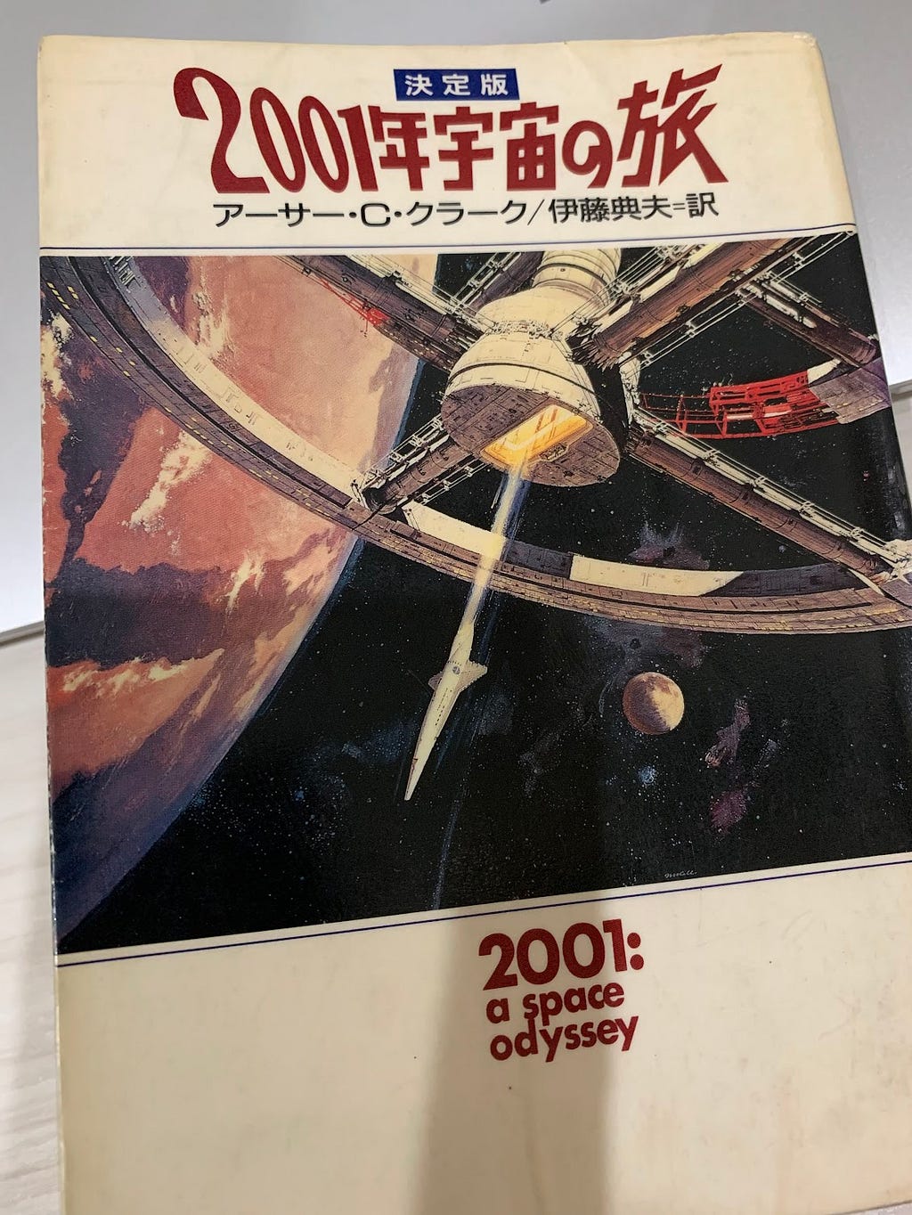 A photo of the Japanese edition of ‘2001: A Space Odyssey’ by Arthur C. Clarke. The cover features an illustration of a massive space station orbiting a planet, with a spacecraft docking at its center.