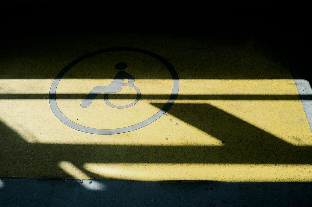 An image of a disabled icon painted on the street in yellow. The icon is covered by shadow.