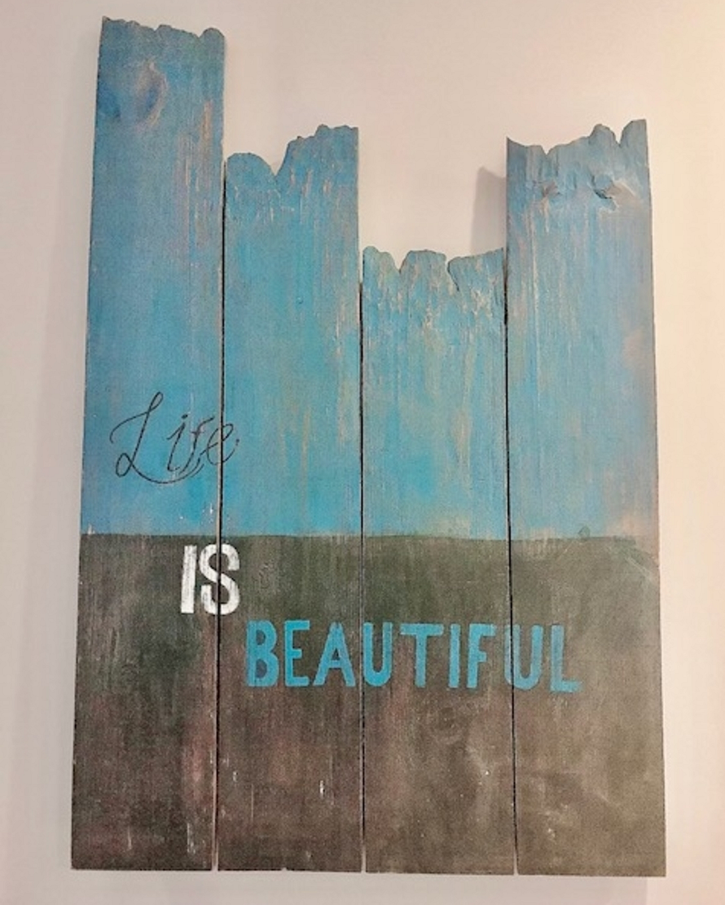 A piece of wood panels with turquoise blue at the top and gray  at the bottom, with the wordings of ‘Life Is Beautiful’ in the center.