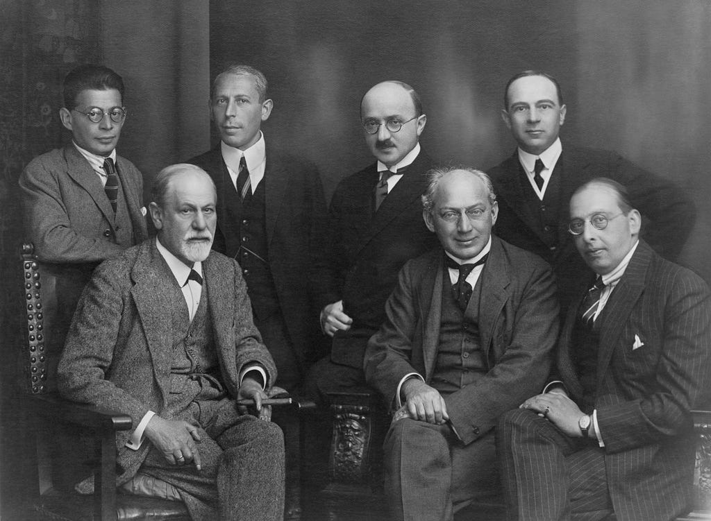 Black and white photograph of seven mature and older men in suits, sitting and standing