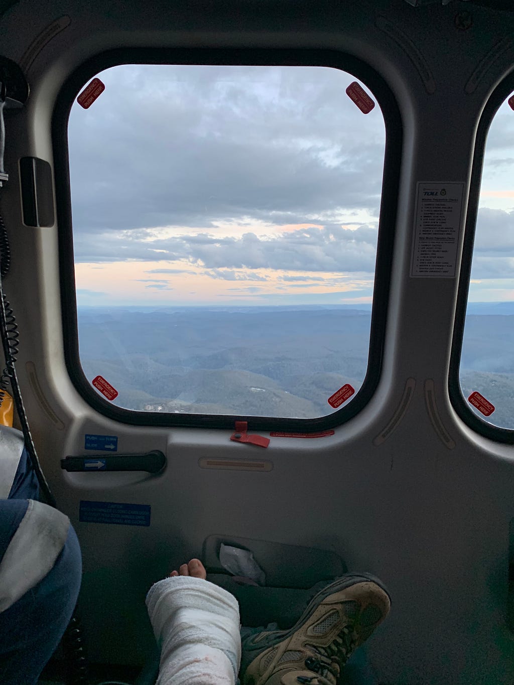In a helicopter. There’s two feet. One is bandaged the other is wearing a boot. There’s beautiful mountains in the view.