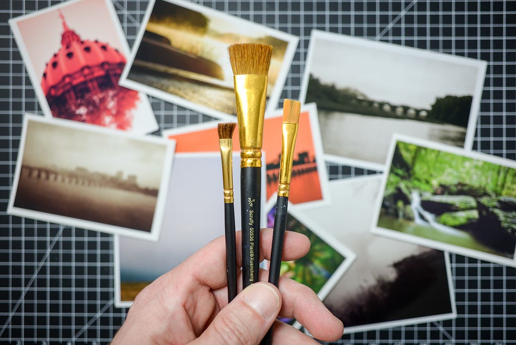 A hand holding a set of paintbrushes over a set of photographs.