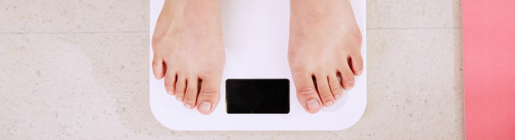 Close up of a weighing scale with a pare of male feet on it.