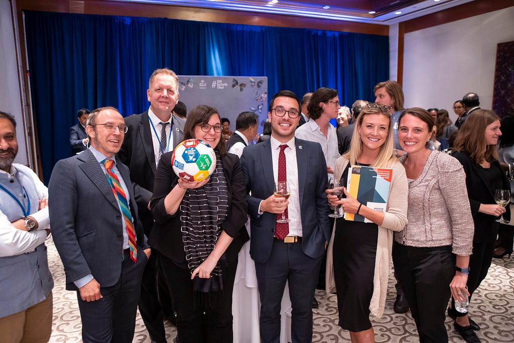 A group of six individuals at the evening reception, one of which is holding an SDG soccer ball.