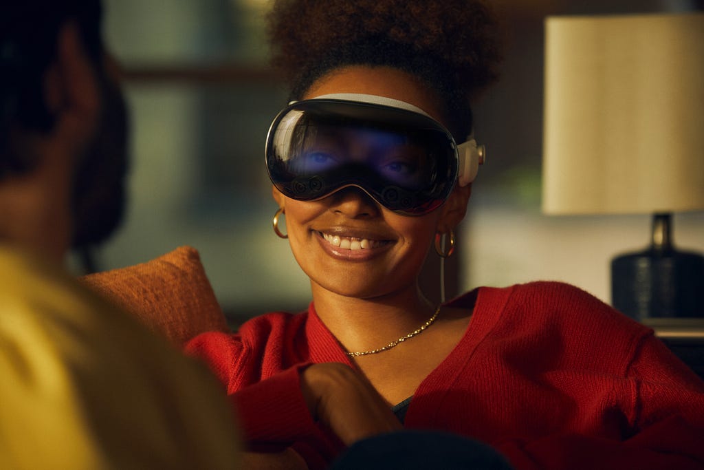 A woman wears the Apple Vision Pro as she speaks to a man beside her