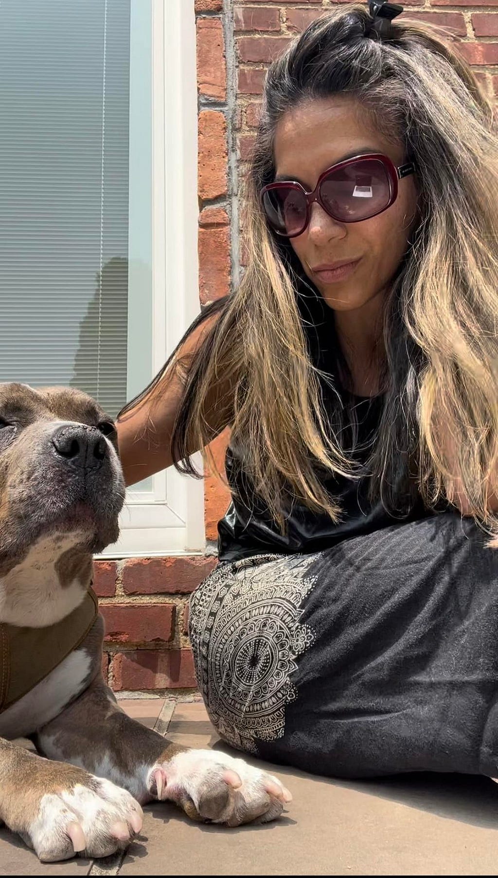 Woman of color on door step with black outfit and petting a dog.