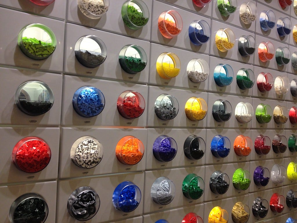 A photograph of the lego blocks in a lego store, they are in plastic bubbles in a wall and are organized by color groupings