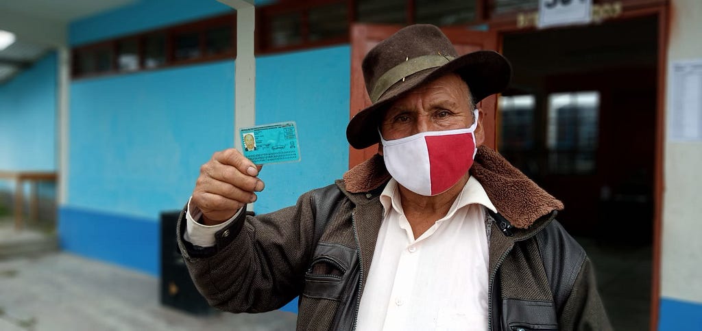 A older man wearing fedora holds his voter identification card.