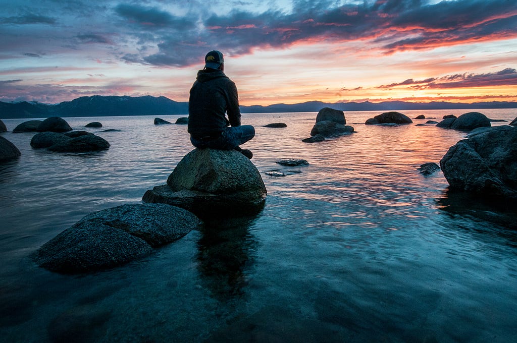 Person sitting on a rock overlooking a beautiful sky and lake.