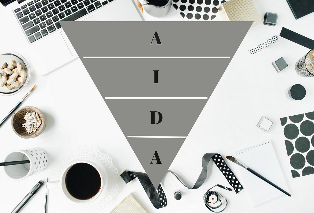 A white desk with a laptop, black and white stationery, and a cup of coffee with a gray pyramid above and the AIDA acronym inside