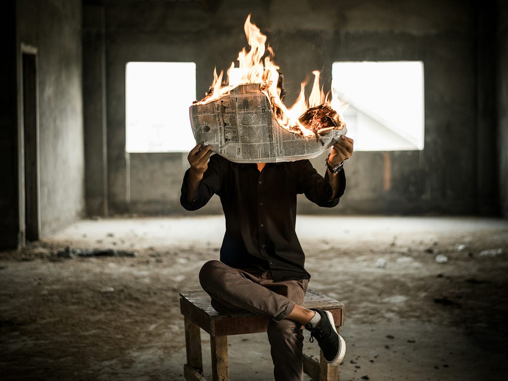 Person sitting on a stool reading a newspaper that is on fire
