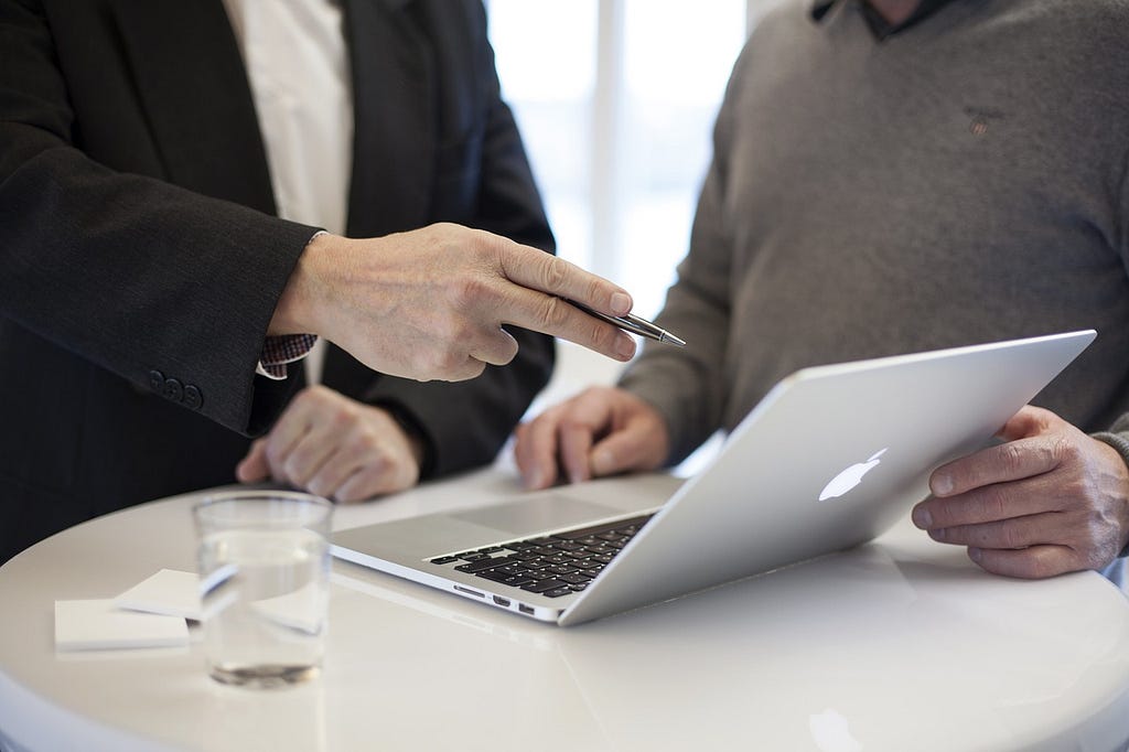 A photo showing a hand point to the screen of a laptop, while another hand (belonging to another person) holds the screen. The image is used to illustrate someone making use of the professional services that belong to another.