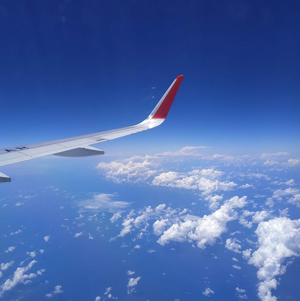 A wing of an airplane over the Caribbean sea, with clouds and a clear blue sky