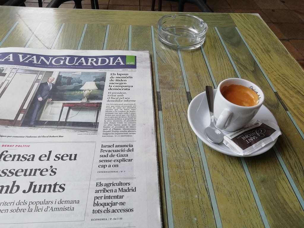 A newspaper sits on a cafe table, next to a cup of coffee