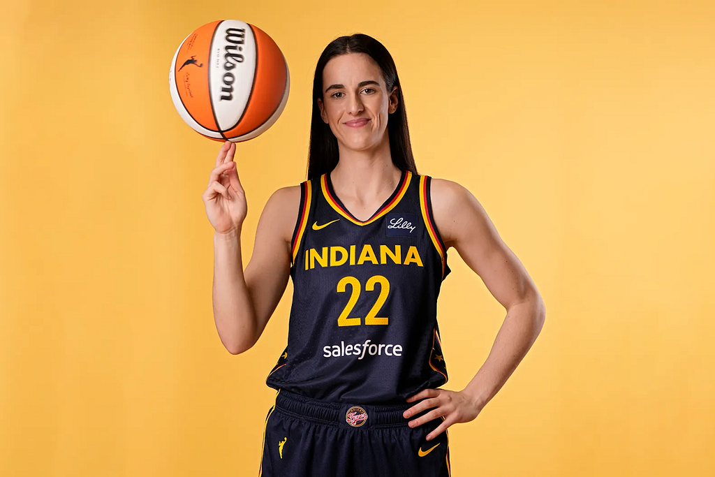 Photo of Caitlin Clark in her Indiana Fever jersey and twirling a orange and white basketball on her right middle and index fingers.