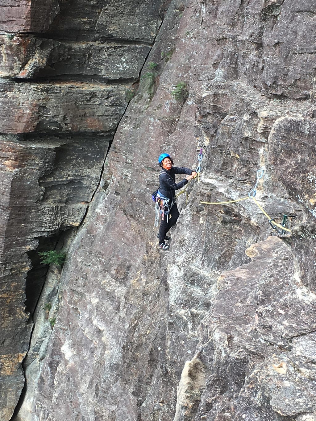 A woman rock climbing. She’s smiling and wearing a helmet