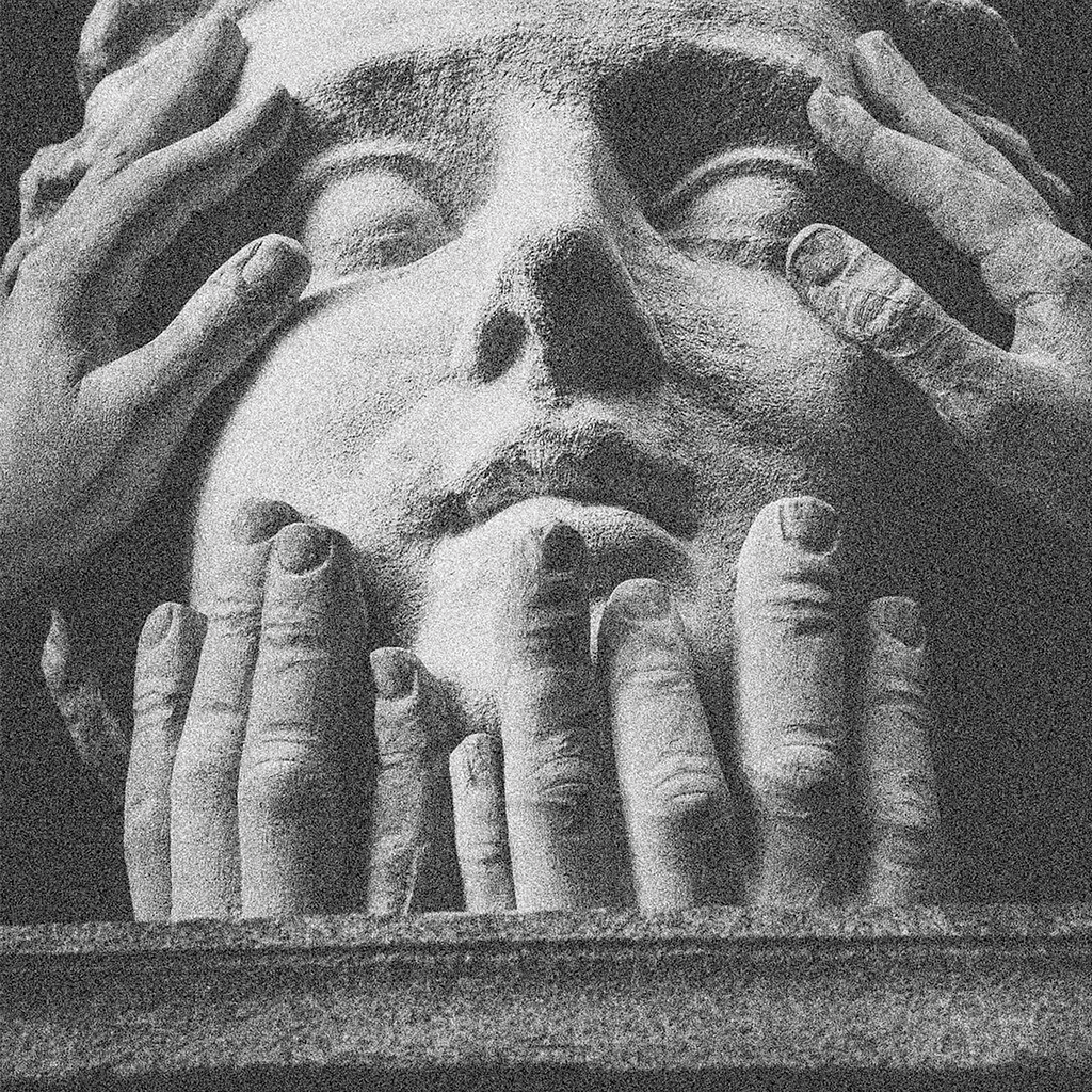 Close up of stone sculpted hands and fingers around the face of a stone sculpted statue