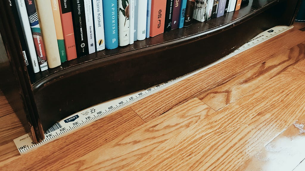 Photo of a yardstick wedged underneath a bookshelf to keep it level
