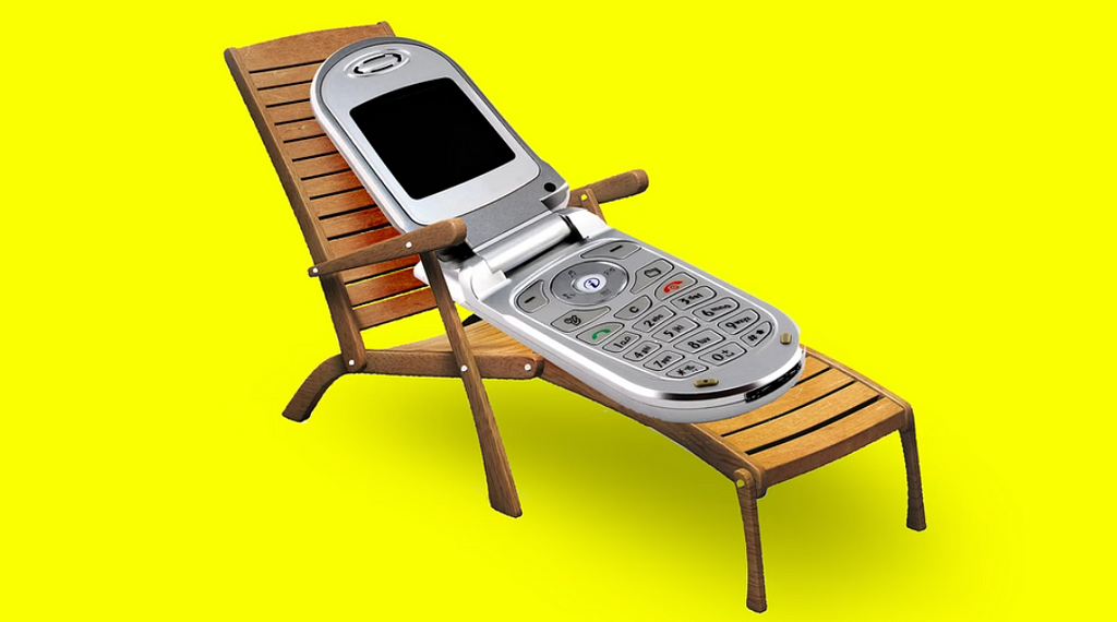 A flip phone lies relaxing on a pool chair over a bright yellow background.