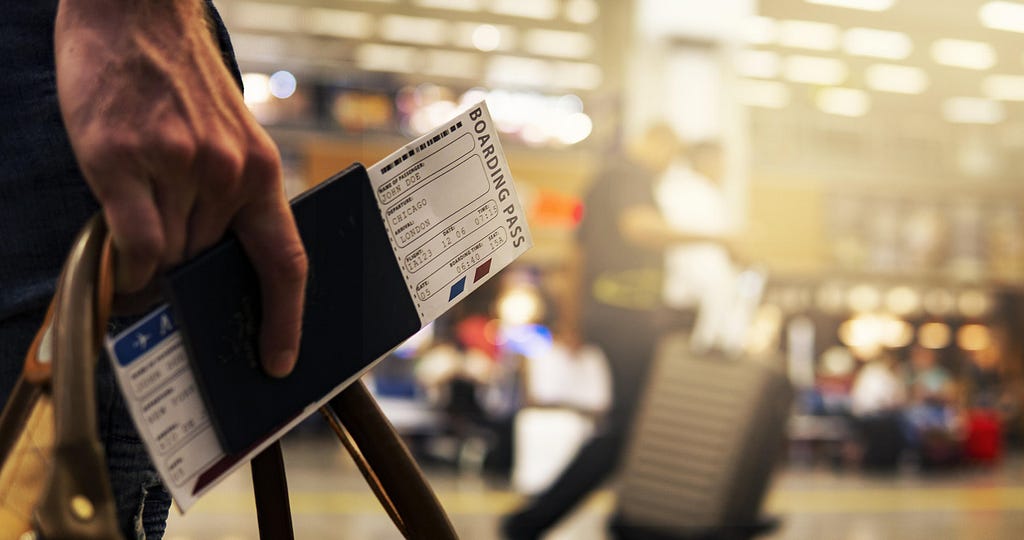 A hand holding a passport with a boarding pass and a travel bag on an airport lounge background