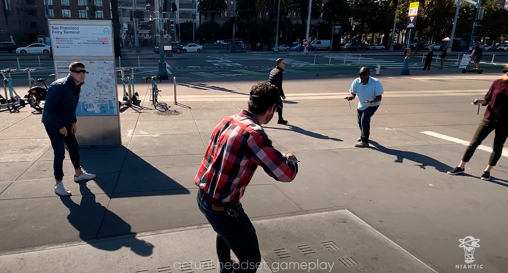 The image shows a group of people outdoors, engaging in AR gameplay while wearing headsets. They appear to be interacting with virtual elements not visible in the photo.