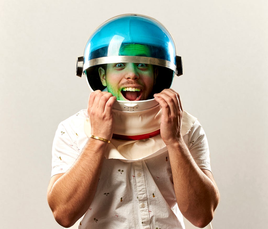 Man wearing a white button down shirt and a space helmet. The visor is open and his face looks surprised.