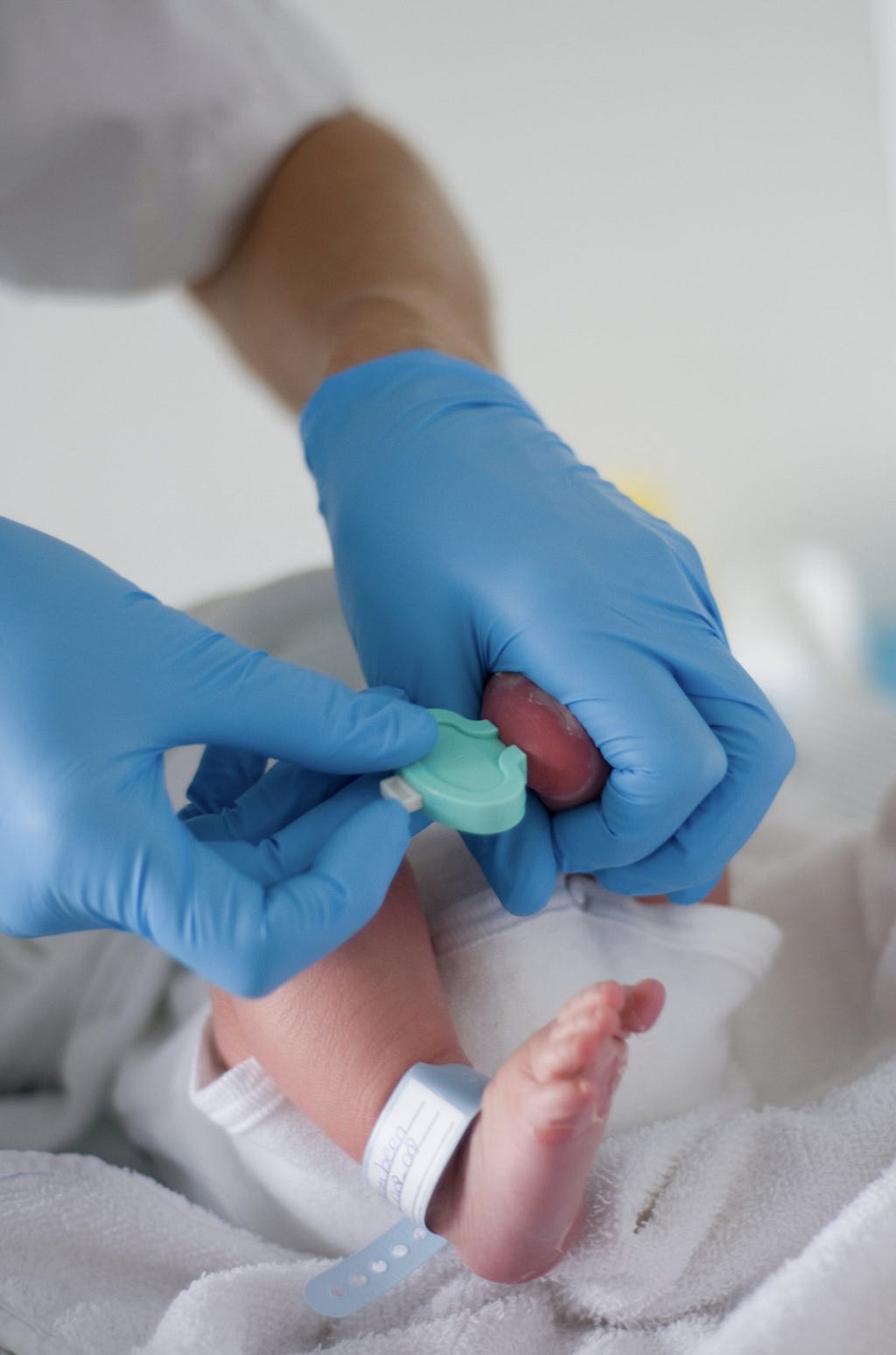 Two hands in blue medical gloves take a blood sample from a newborn’s heel.