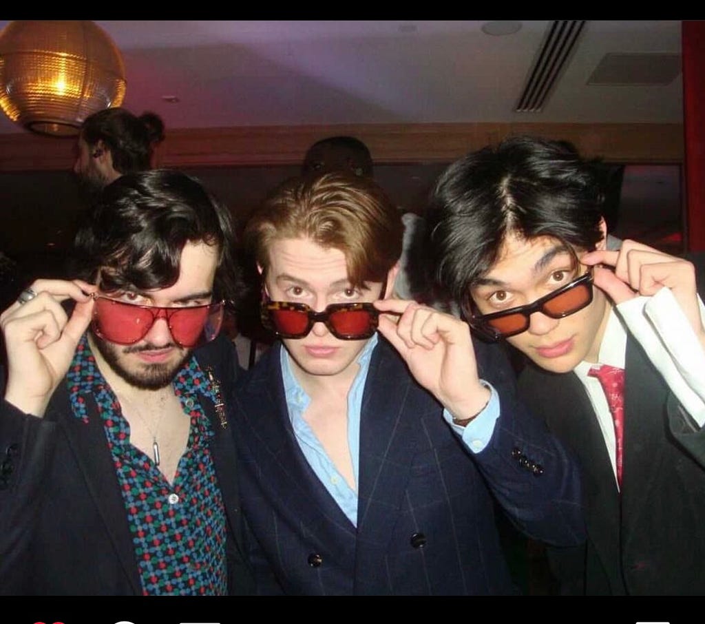 Kit and his co-stars staring at the camera with tinted red-sunglasses