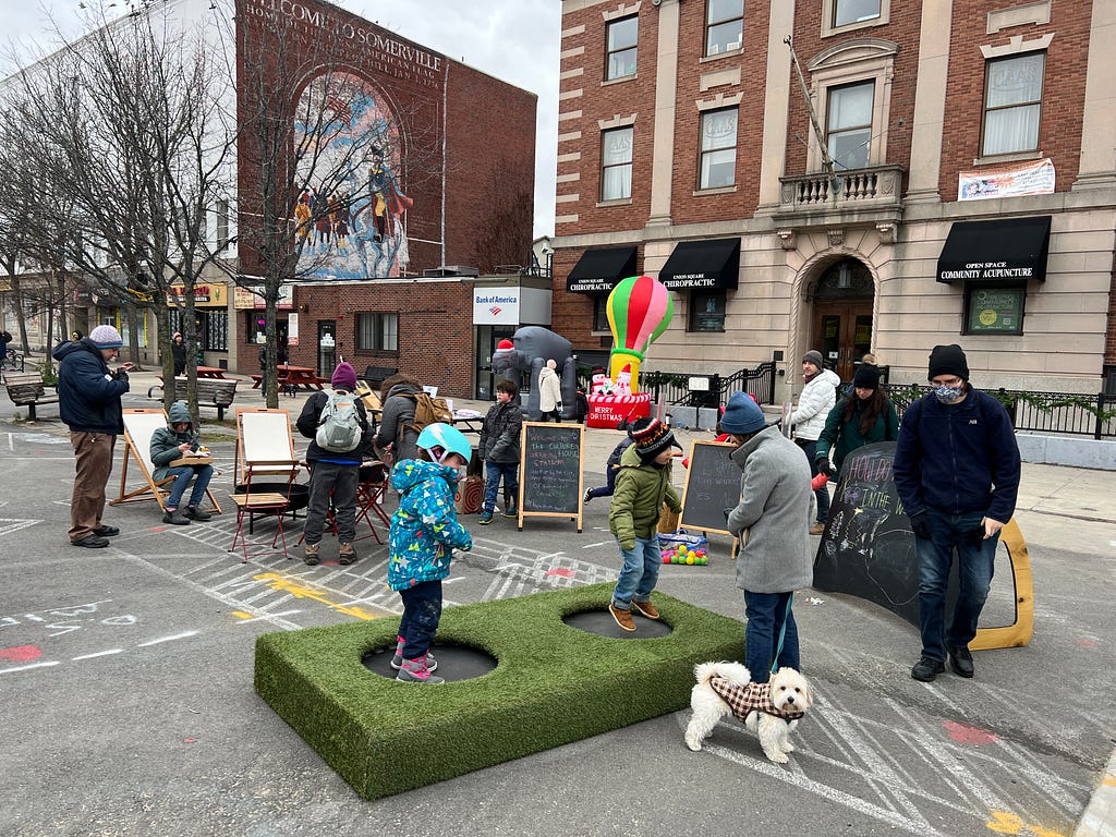 A group of visitors of all ages gather at our pop-up featuring a trampoline, chairs to sit, a firepit, a s’mores station, and chalkboards to write or draw on.
